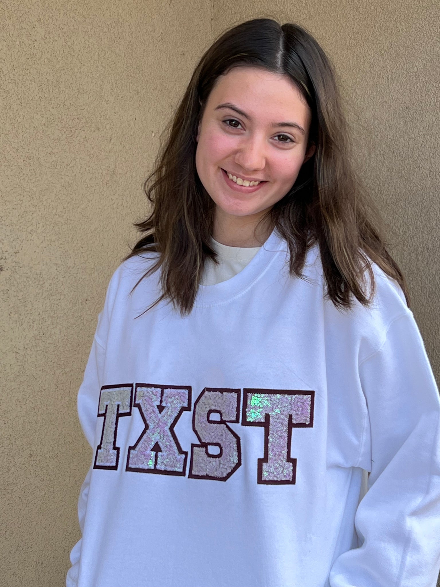 TXST Iridescent Sequined Stitch Letter with Maroon Background on a White Sweatshirt